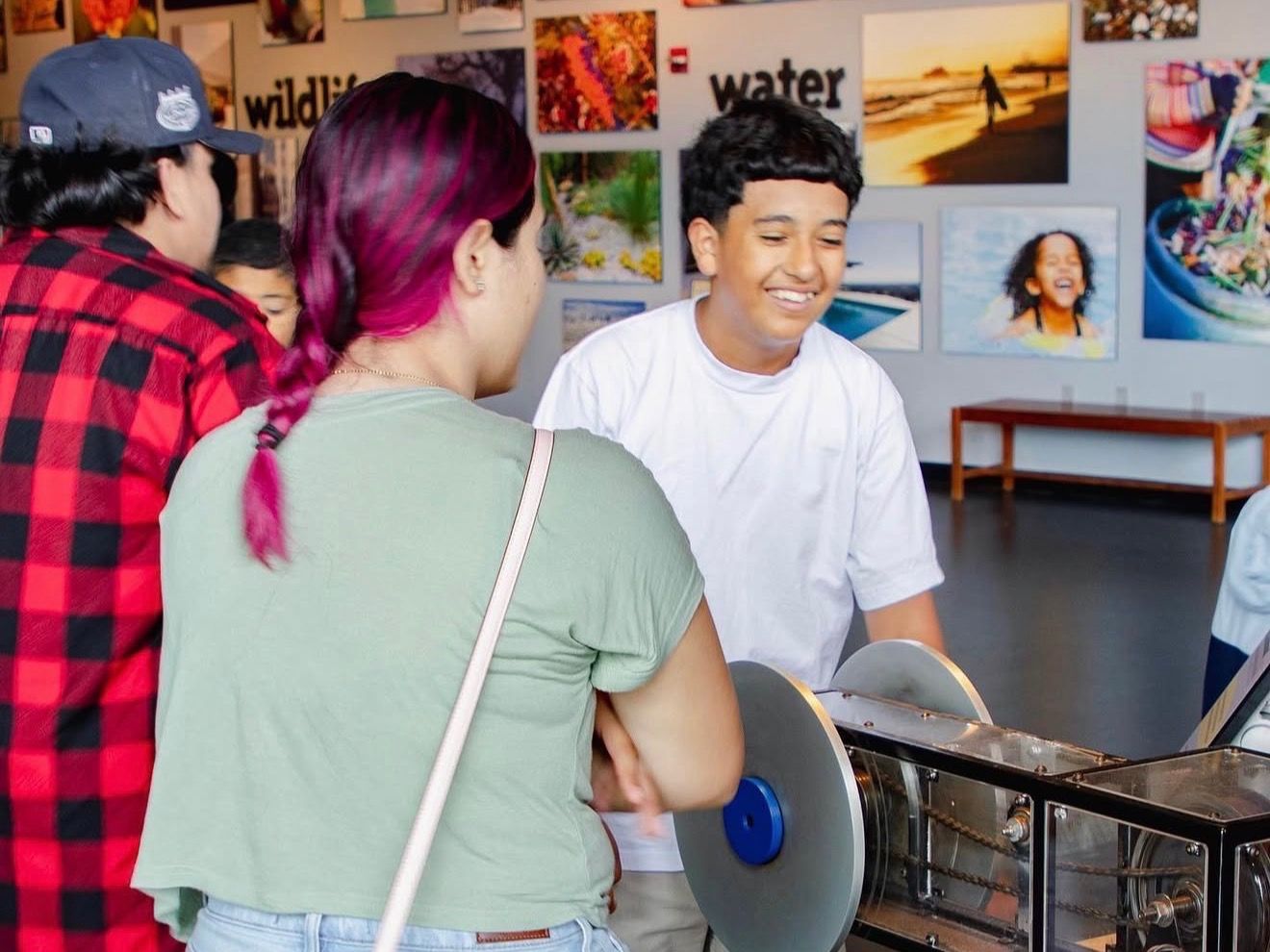 Students at a hands-on exhibit; one smiles as he turns the crank of a large machine.